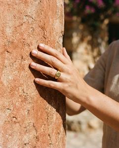 Mano con un anillo de sello dorado sobre un muro de color teja